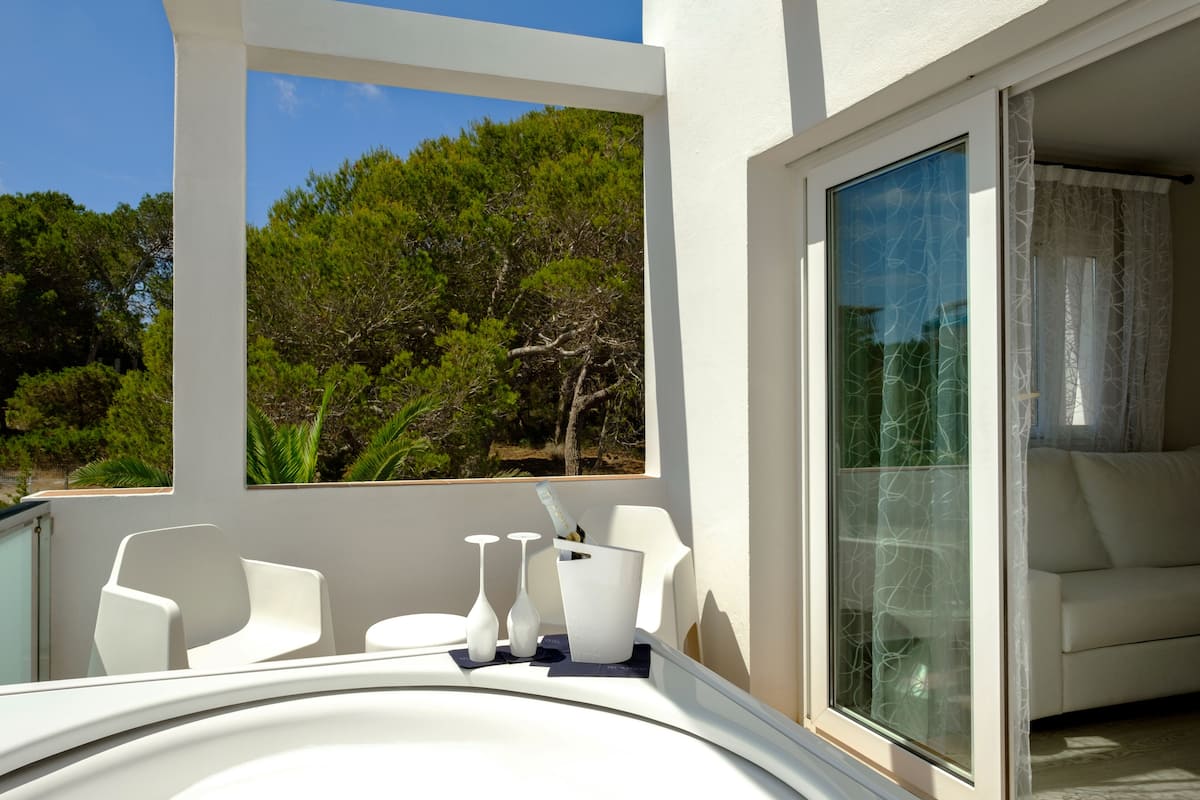 Un balcón moderno con mobiliario blanco, incluyendo sillas y una mesa, con vistas a un paisaje verde y exuberante.