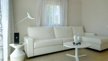Una sala de estar moderna con un sofá blanco, una mesita redonda pequeña, una lámpara de pie y una ventana con cortinas translúcidas.