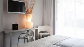 Una habitación de hotel moderna con cama, escritorio con silla, televisor de pantalla plana y un florero con plantas secas.