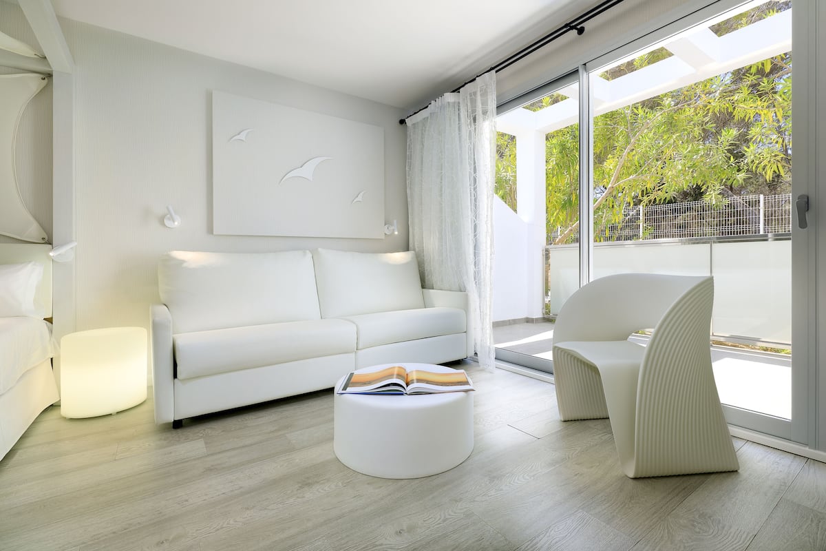 Una sala moderna con un sofá blanco, un otoman redondo con un libro y una silla blanca.