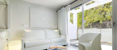 Una sala moderna con un sofá blanco, un otoman redondo con un libro y una silla blanca.