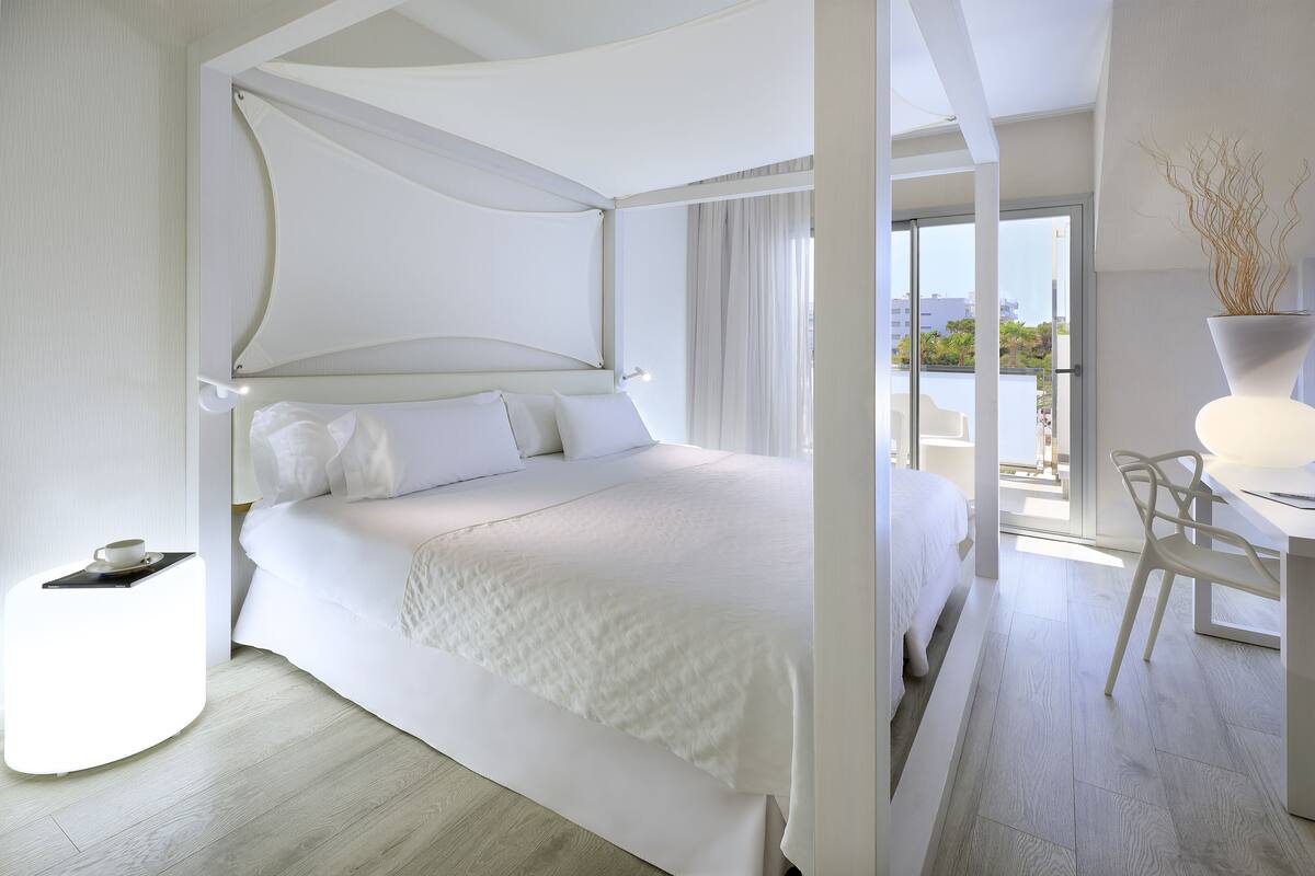 Una habitación de hotel moderna con una cama grande, una mesita con una taza y vistas al exterior.