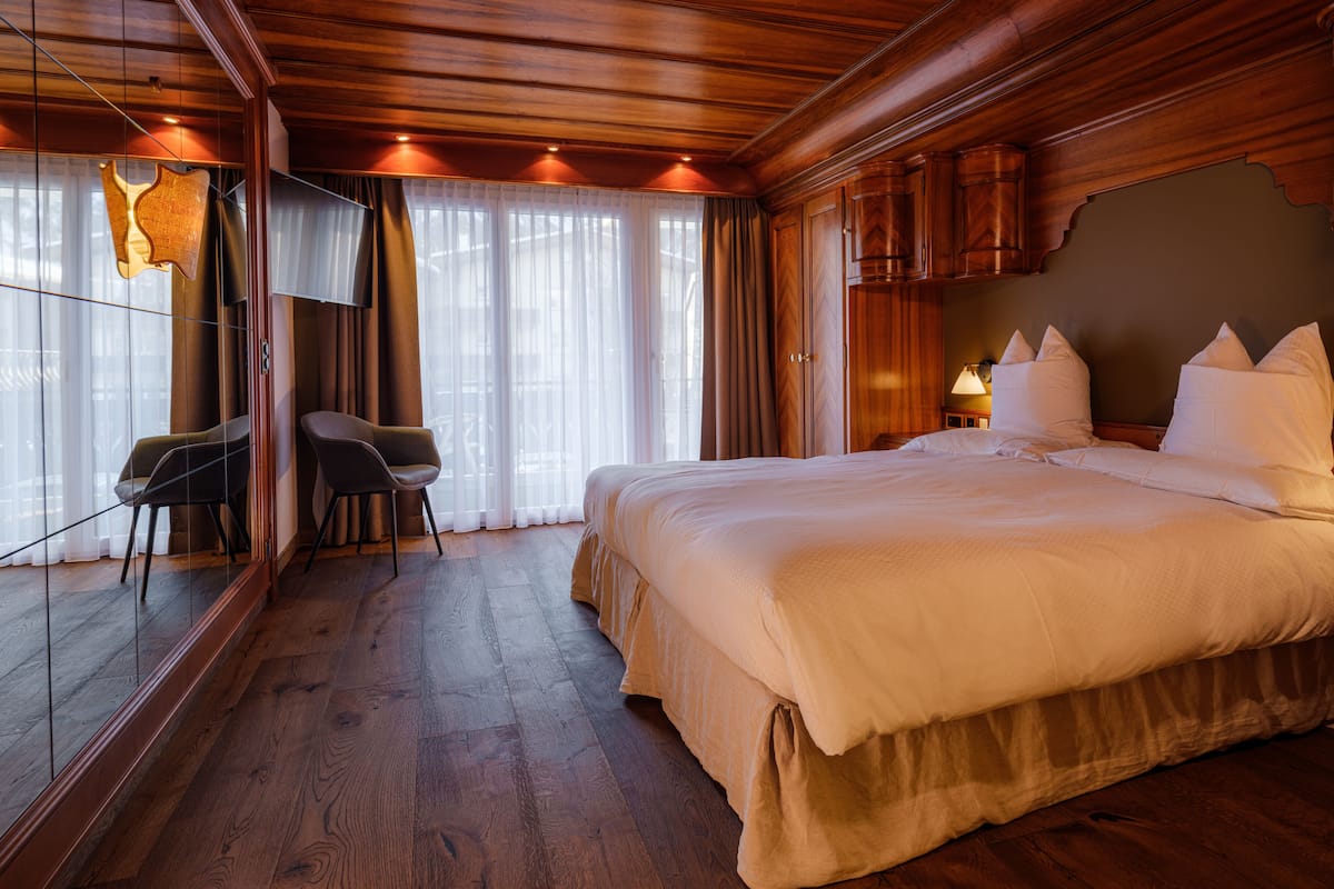 A hotel room with a large bed, wooden flooring, a seating area with chairs, and a large mirror.