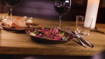 Una mesa de madera con un plato de comida, una copa de vino tinto y una vela.