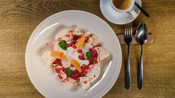 Un plato de postre con fruta y crema sobre una mesa de madera, acompañado de una taza de café y cubiertos.