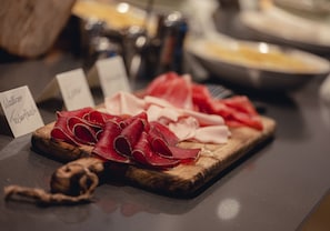 Une planche en bois sur laquelle sont présentées différentes sortes de charcuteries, notamment du salami et du jambon cru, et qui est posée sur un comptoir.