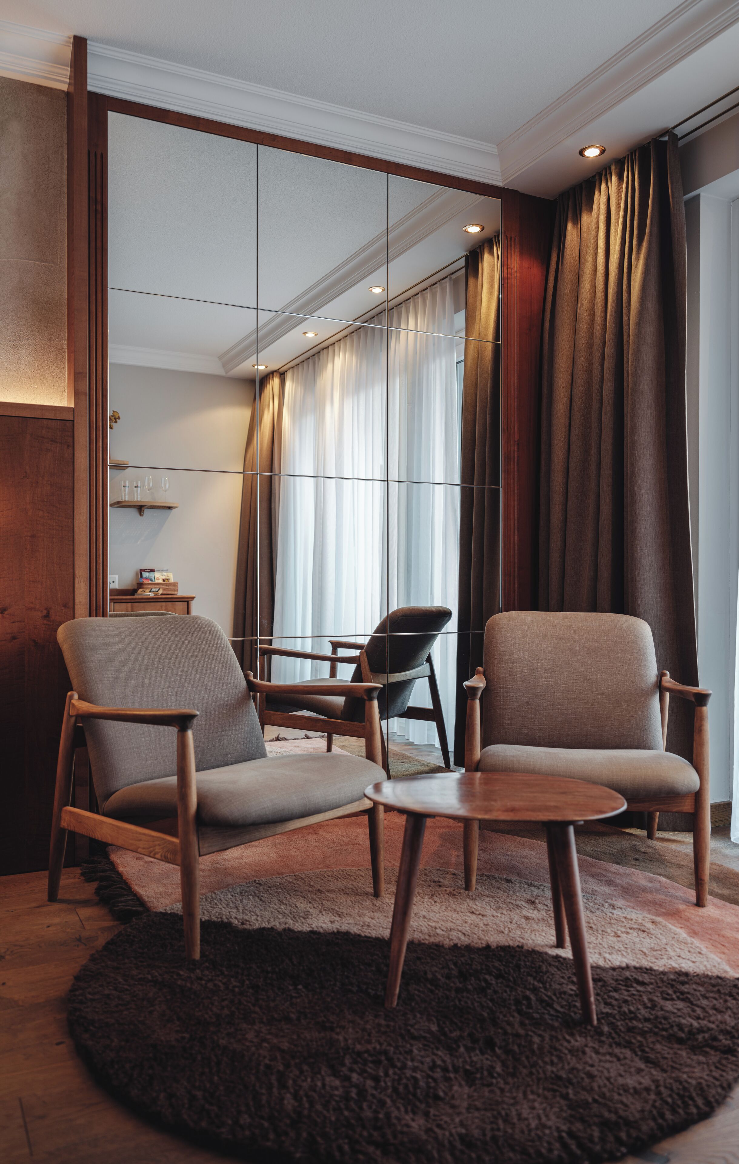 Une pièce moderne avec deux fauteuils, une petite table et un grand miroir.