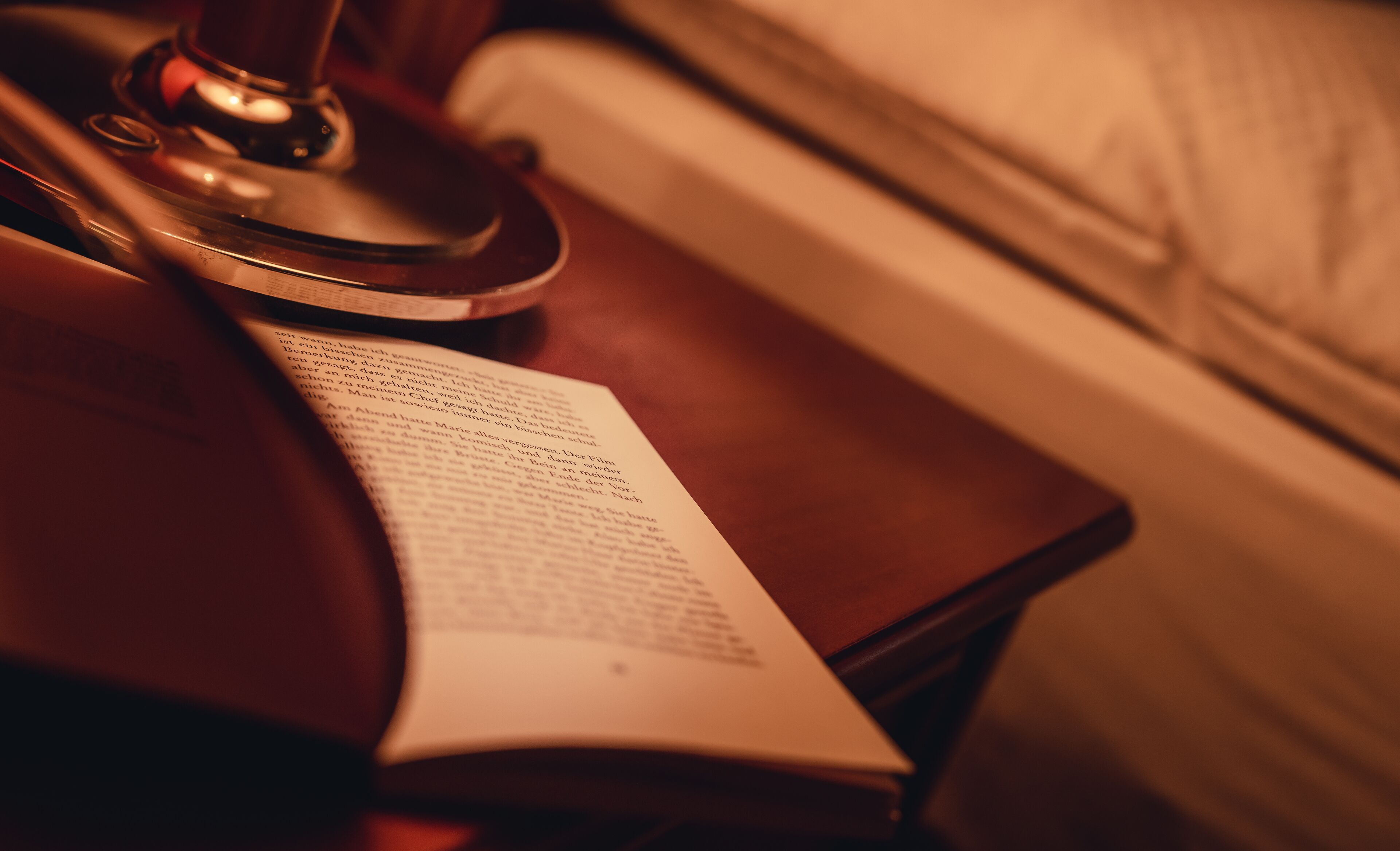 A book on a wooden table next to a lamp.