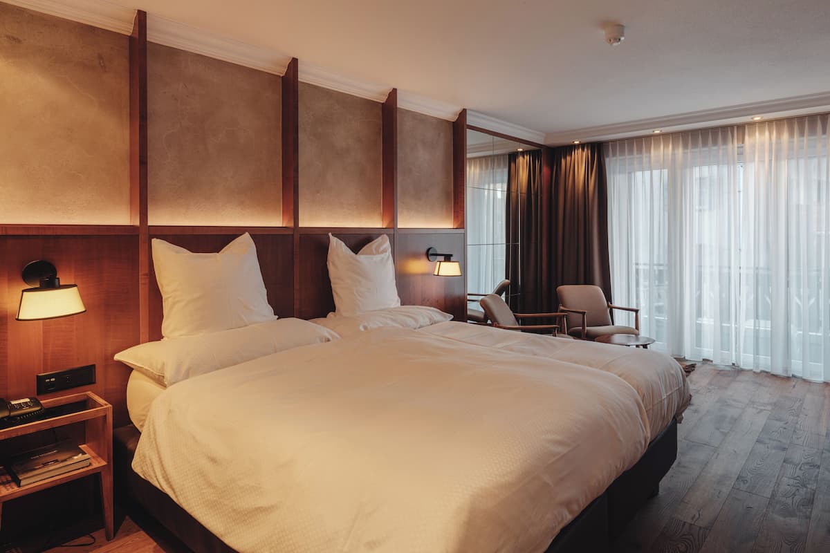 A hotel room with a large bed, a desk, a chair, and a window with curtains.