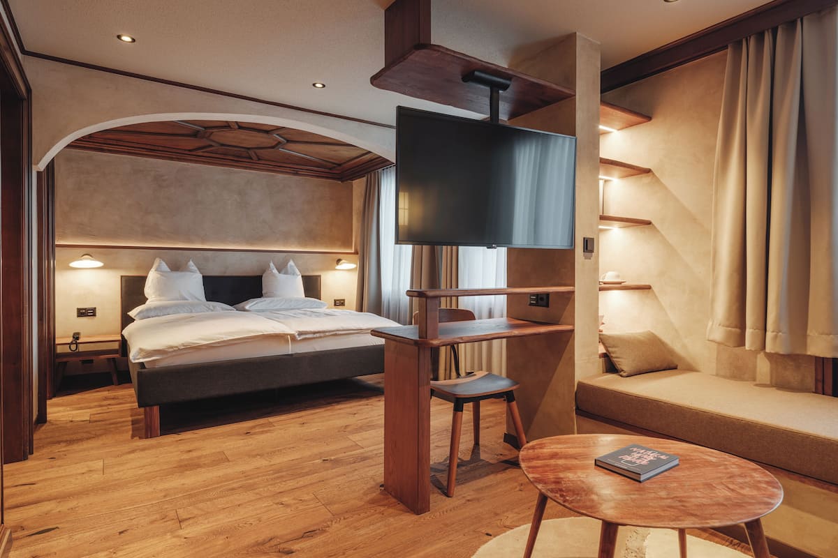 A modern hotel room with a large bed, a TV mounted on a wooden stand, a small table, and a sofa.