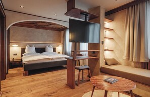 A modern hotel room with a large bed, a TV mounted on a wooden stand, a small table, and a sofa.