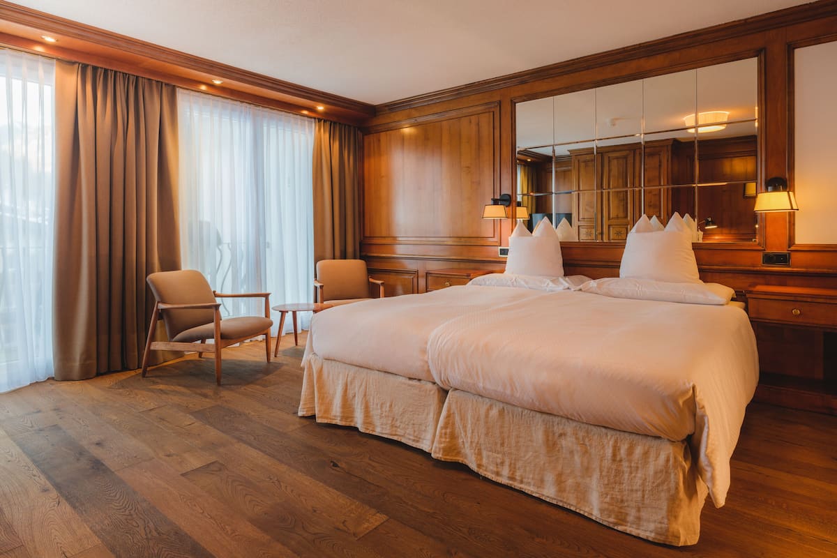 A hotel room with a large bed, two chairs, a desk, and a mirror.