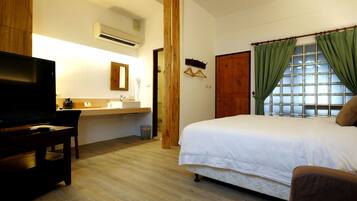 A bedroom with a bed, a TV, a wooden desk, and a bathroom visible in the background.