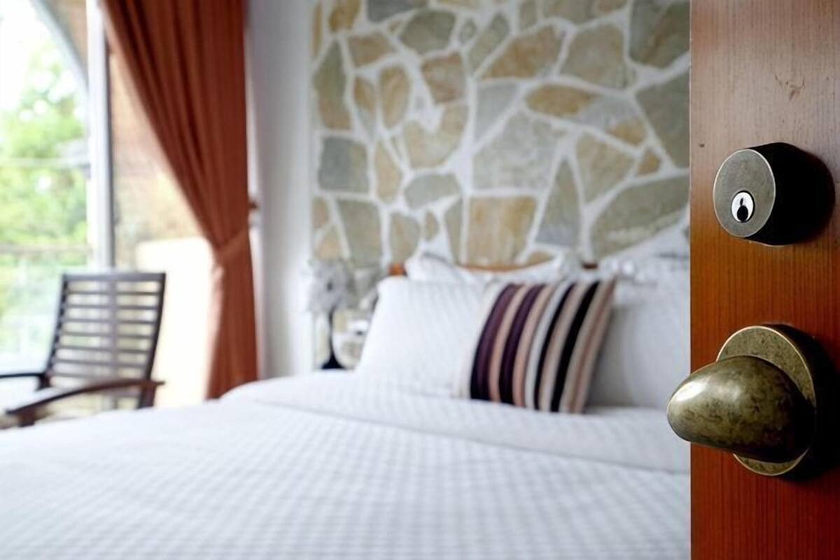 A bed with a stone wall behind it, a door with a lock, and a chair in the background.