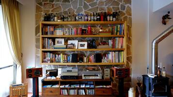 A cozy living room with a stone wall, wooden bookshelves filled with books and decorative items, a vintage radio, and a wood-burning stove.