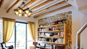 Une pièce avec un mur en pierre, des poutres en bois au plafond, un lustre, une bibliothèque et une cheminée.