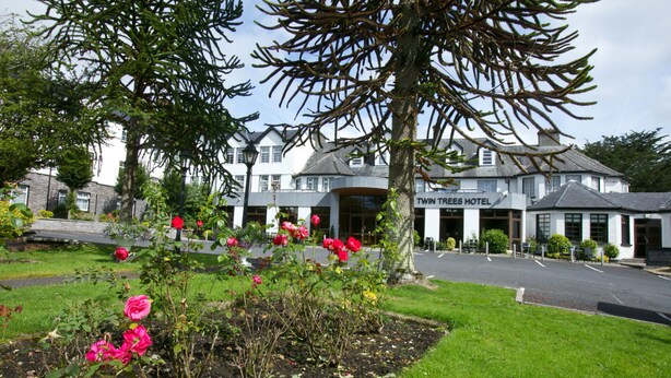 Hotel con jardín delantero, con rosales rosados en flor y césped bien cuidado.