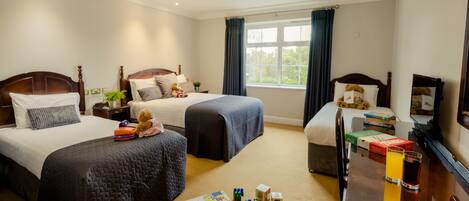 A hotel room with two beds, a TV, a desk with books and a teddy bear, and a window with curtains.