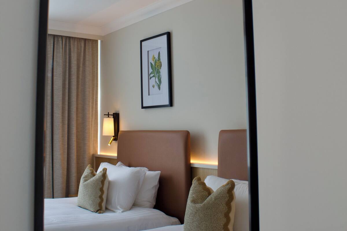 Habitación de hotel con dos camas, un cuadro en la pared y una mesita de noche con lámpara.