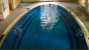 Una piscina interior con agua cristalina, suelo de baldosas y un amplio ventanal arqueado que permite la entrada de luz natural.