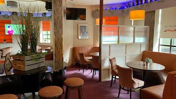 Un restaurante con zona de bar, asientos acolchados y una televisión mostrando un evento deportivo.
