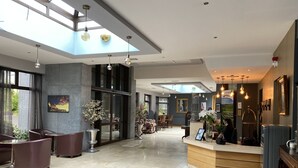 Vestíbulo de hotel con mostrador de recepción, zona de estar y un gran ventanal que permite la entrada de luz natural.