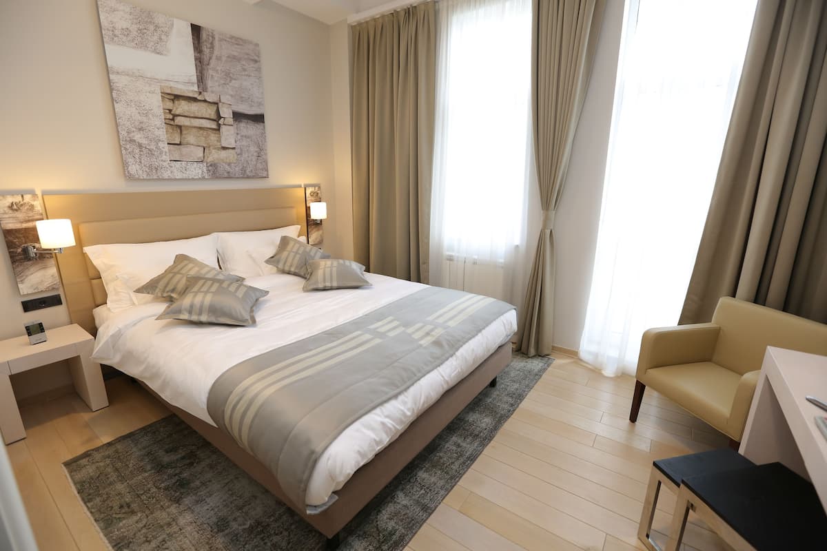 A hotel room with a large bed, a desk, a chair, and a window with curtains.