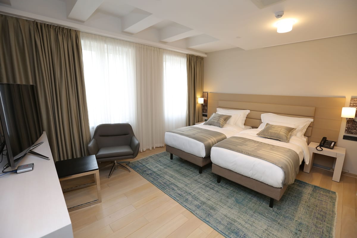 A hotel room with two beds, a desk, a chair, and a television.