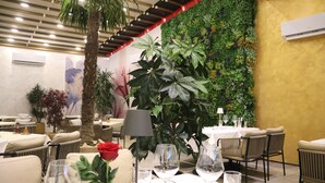 A restaurant with tables set for dining, a decorative plant, and a wall with a green vertical garden.
