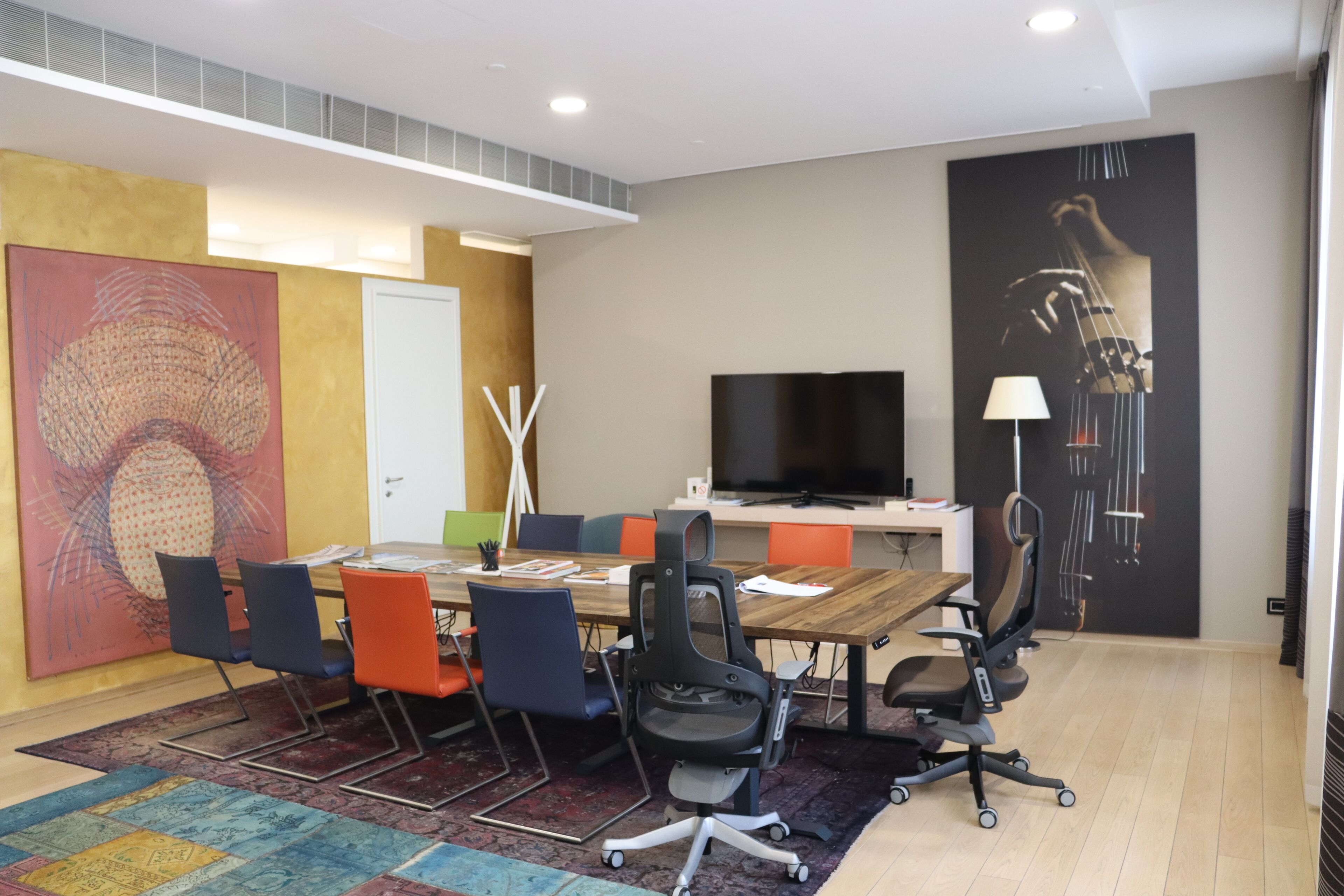 A modern meeting room with a large table, several chairs, a television, and artwork on the walls.