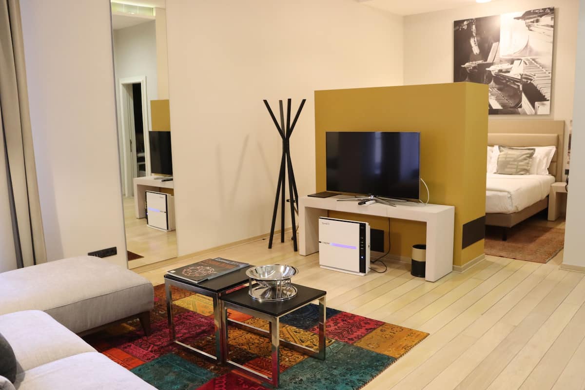 A modern hotel room with a sofa, a TV, a desk with a computer, and a bed.