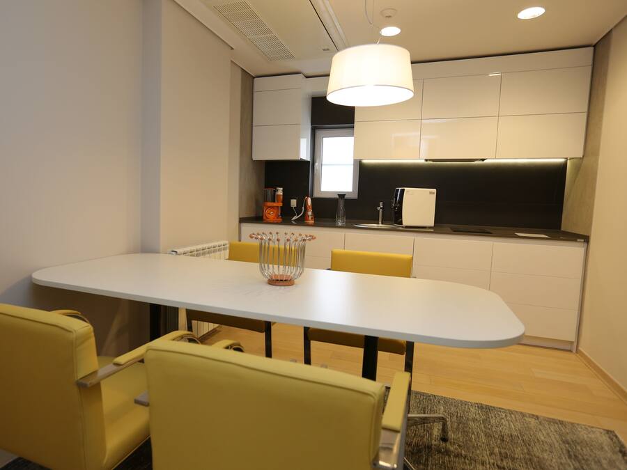 A modern kitchen with a white countertop, yellow chairs, and a large window.