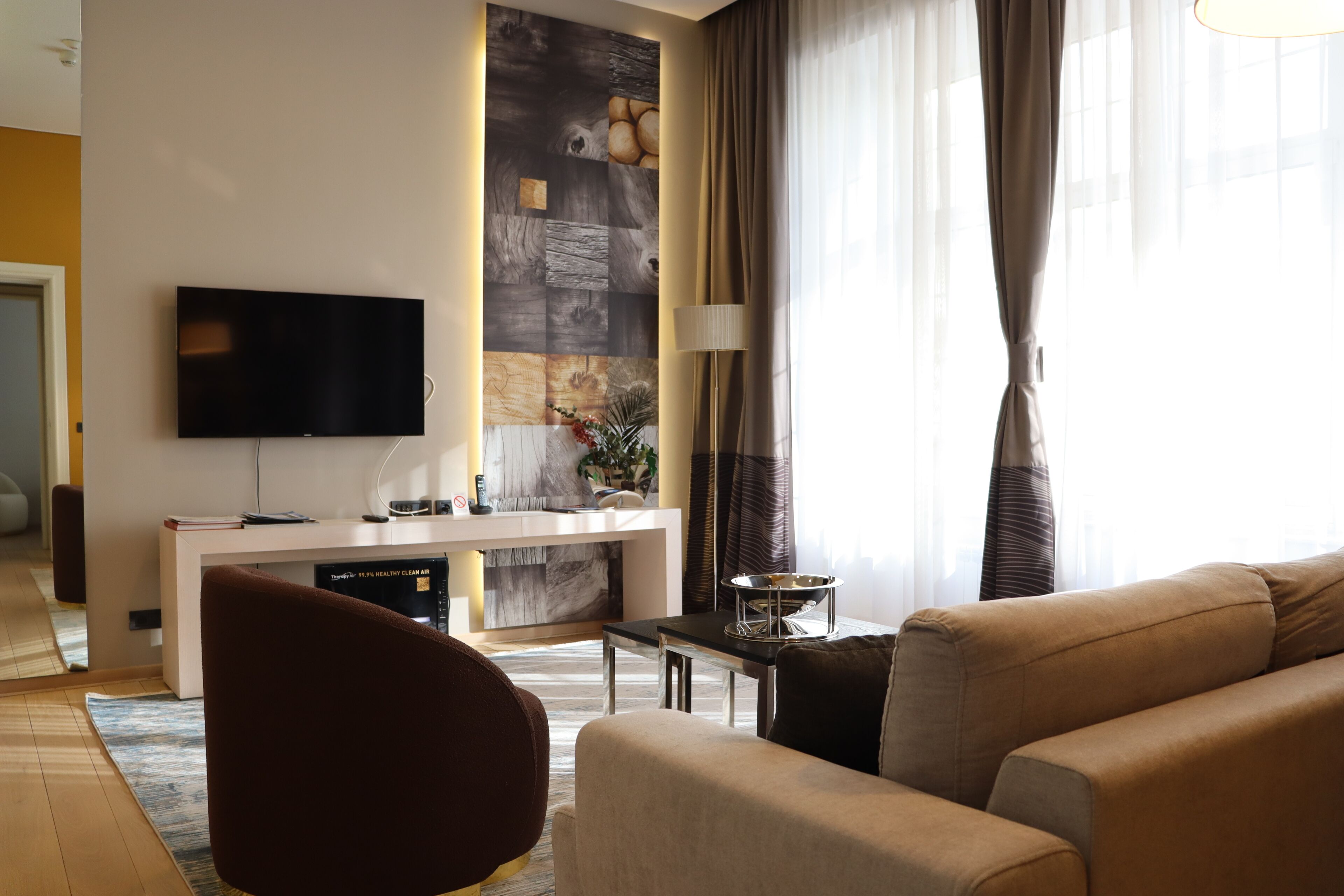 A modern living room with a flat-screen TV, a sofa, a coffee table, and a dining area with a white console.
