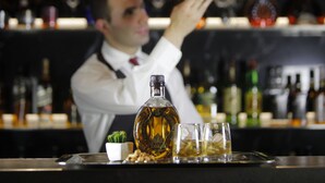 A bartender pouring a drink with a bottle and glasses on a tray.