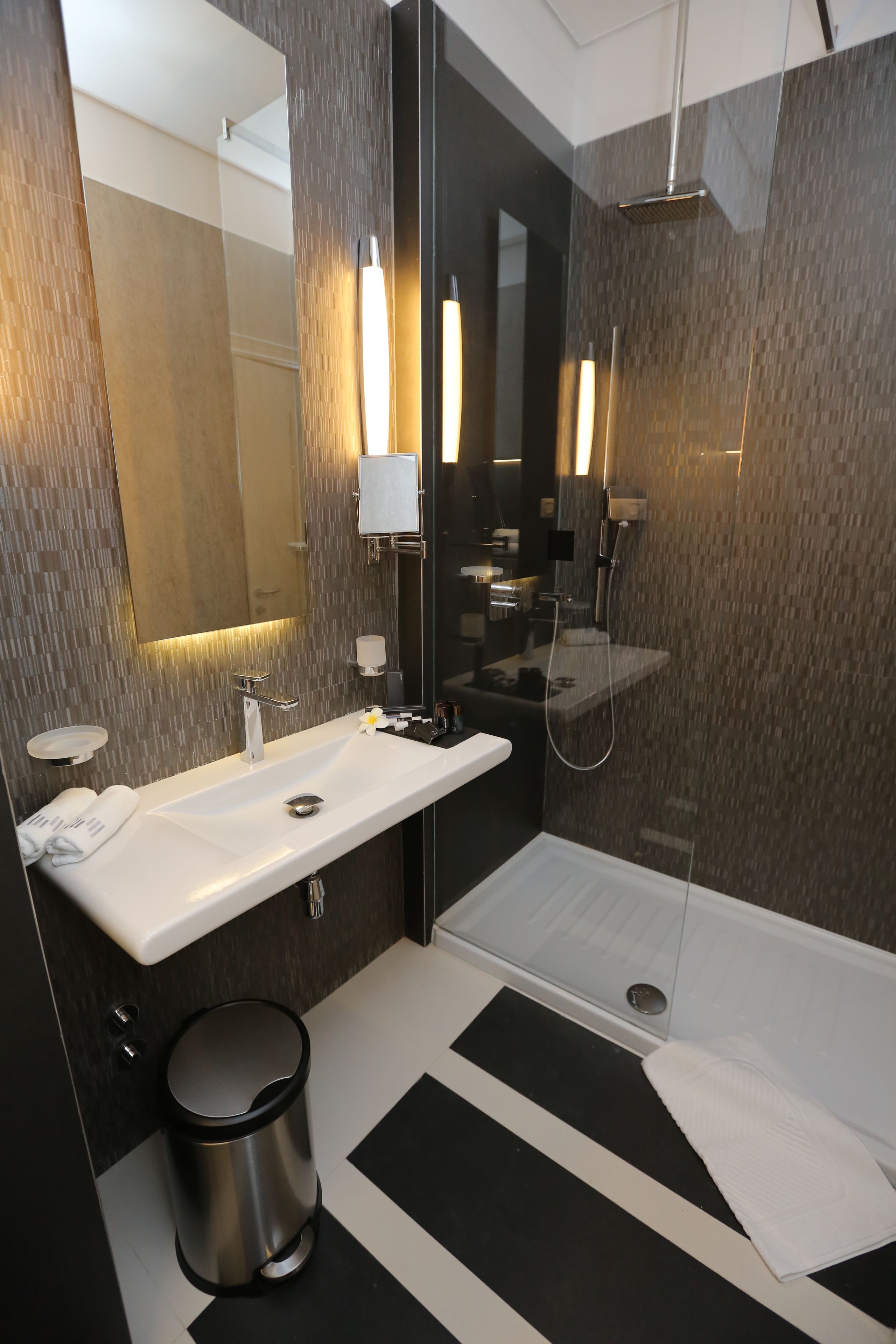 A modern bathroom with a large mirror, a sink, a shower, and a toilet.