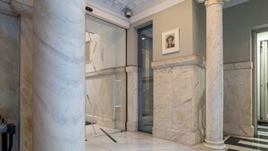 A marble lobby with a glass elevator, a framed artwork on the wall, and a patterned floor.
