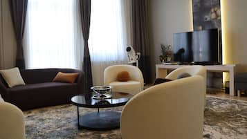 A modern living room with a dark brown sofa, a cream-colored armchair, a round coffee table, and a flat-screen TV.