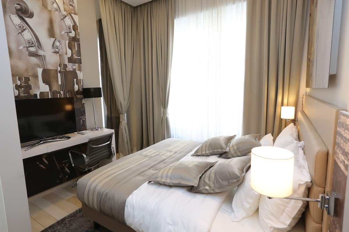 A hotel room with a bed, a TV, a desk, and curtains.