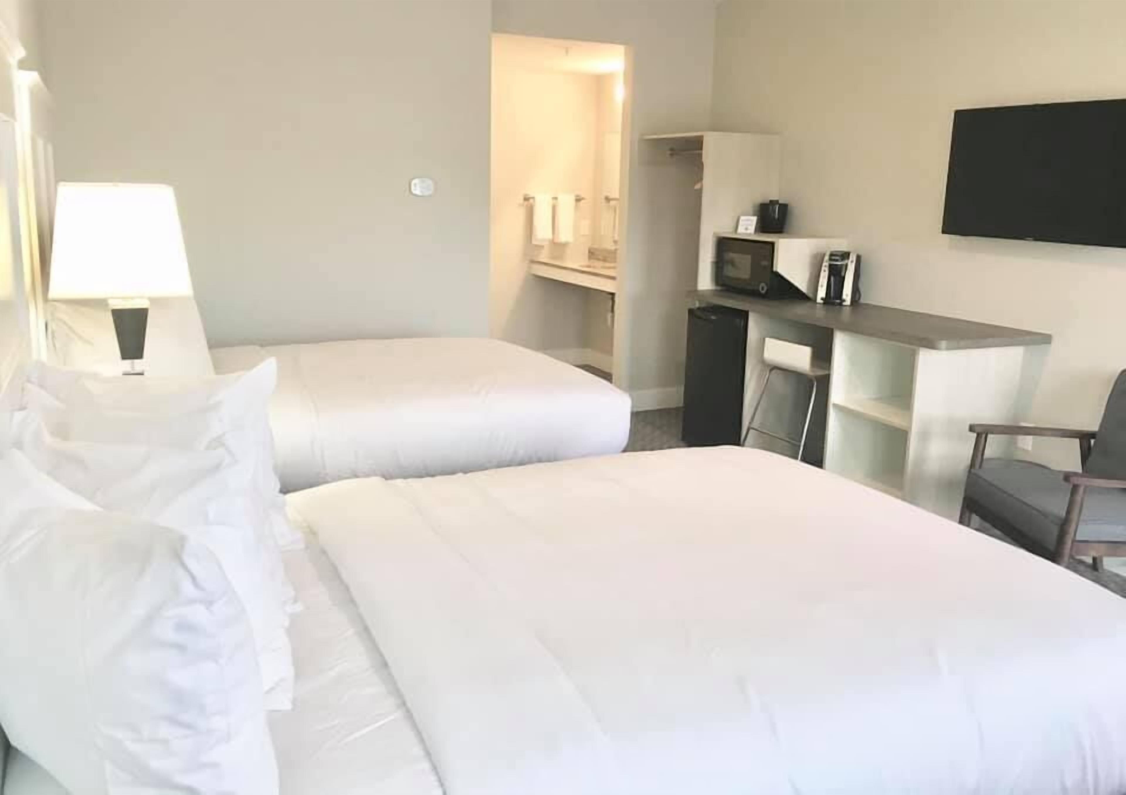 A hotel room with two beds, a desk, a chair, a TV, and a microwave.