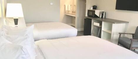 Habitación de hotel con dos camas, un escritorio, una silla, un televisor y un microondas.