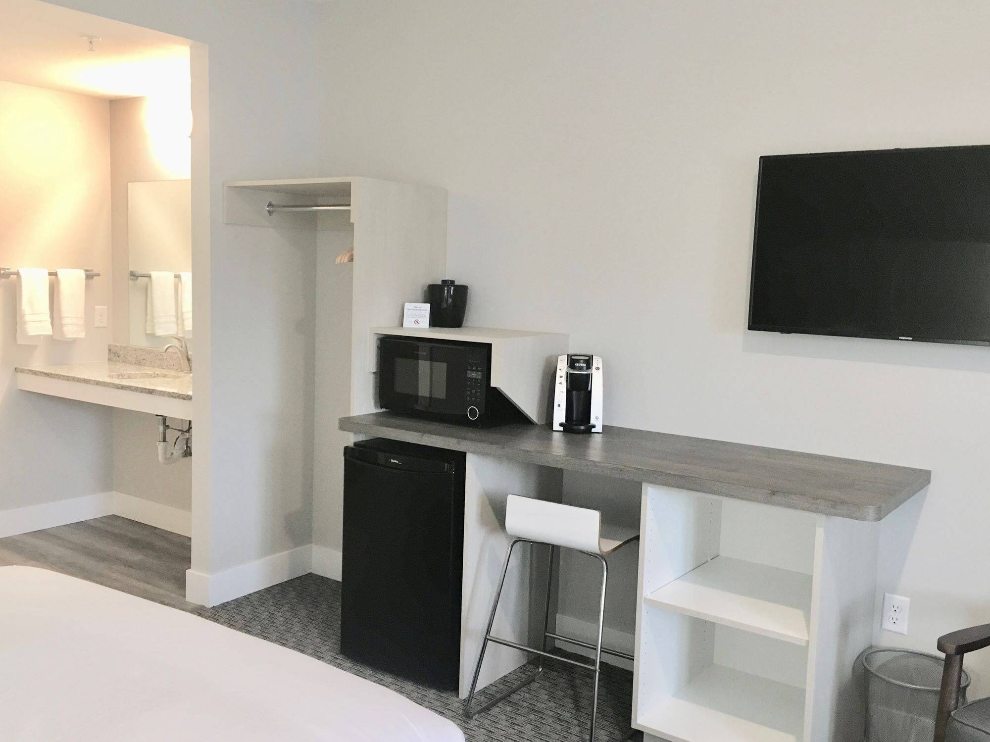 A hotel room with a bed, a desk with a microwave, a coffee maker, and a TV on the wall.