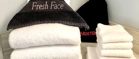A stack of white towels with a black towel on top labeled "Fresh Face" and a black bag with "AIRDRYER" text.