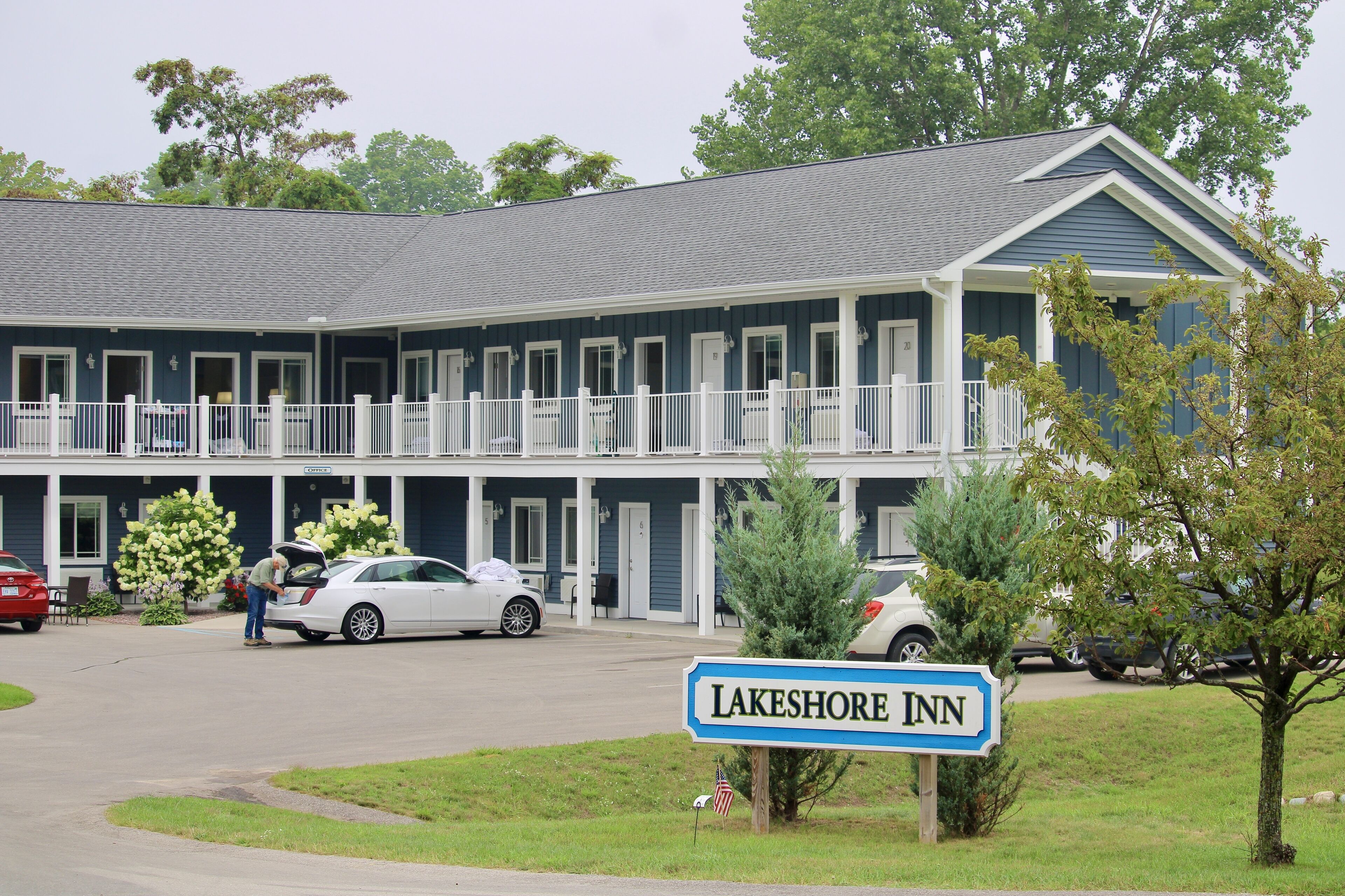 A two-story motel with a blue exterior and white trim, featuring a covered parking area and a sign reading "Lakeshore Inn".