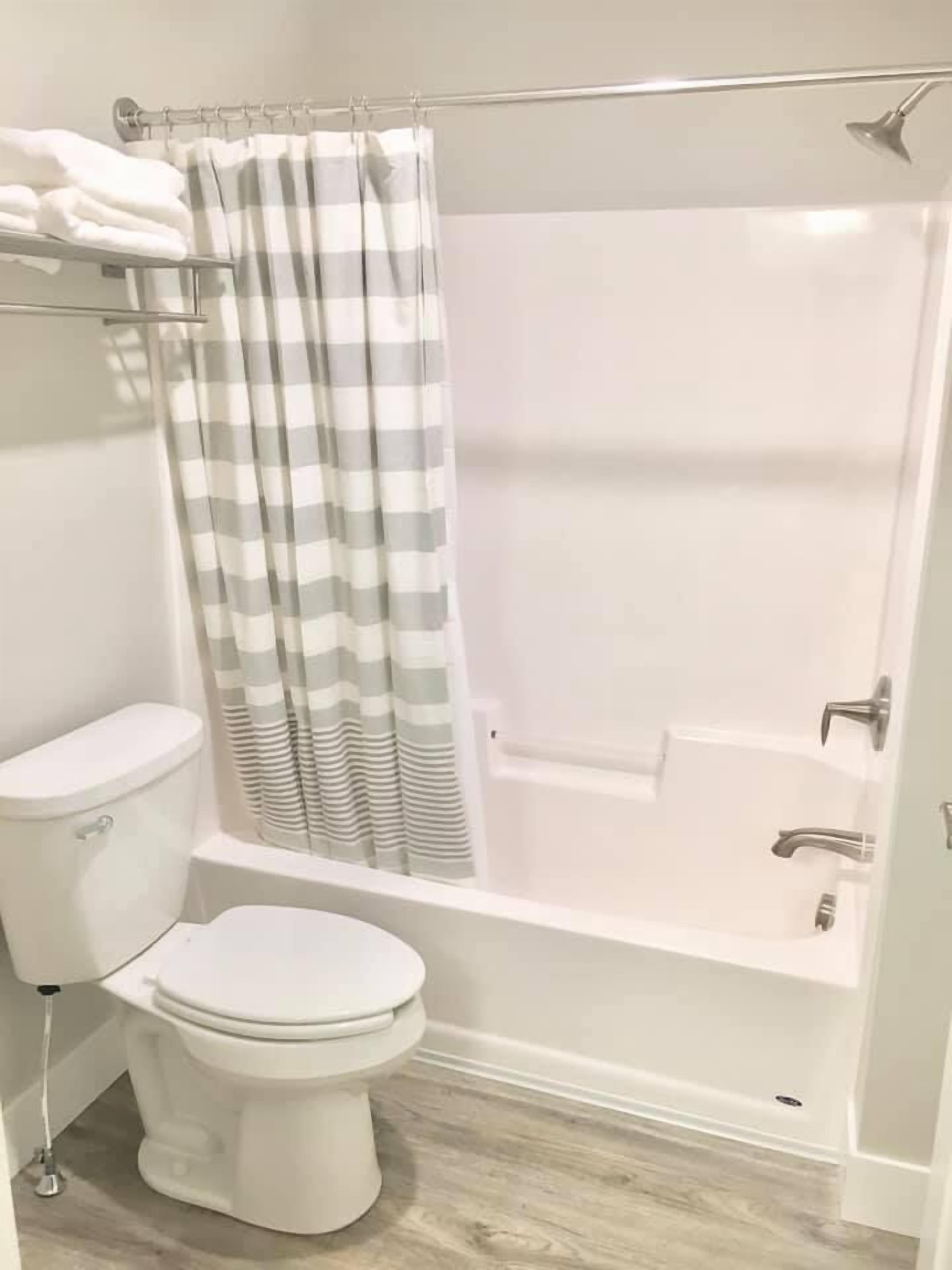 Un baño con inodoro, ducha con cortina a rayas y bañera.