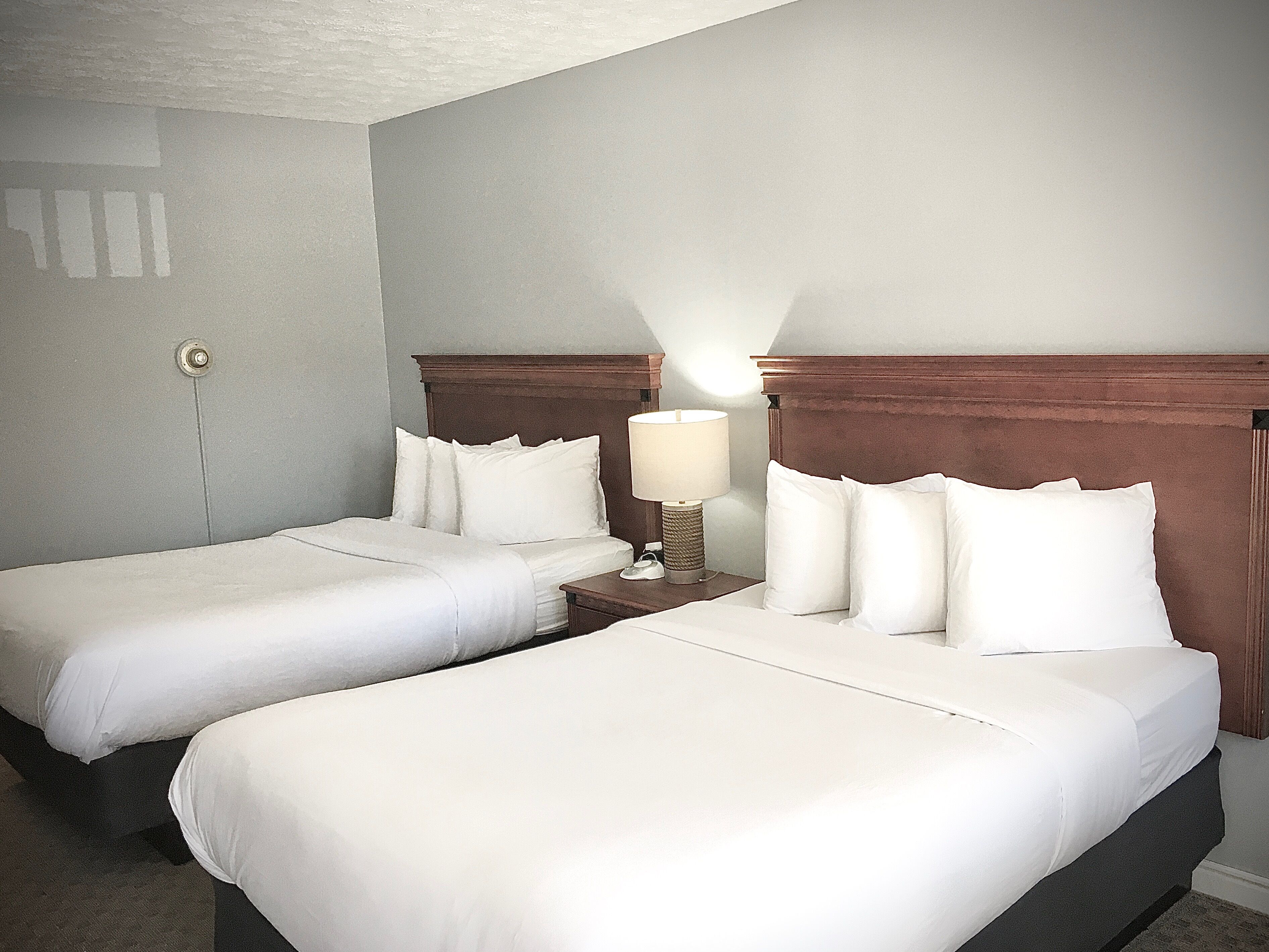A hotel room with two single beds, a nightstand with a lamp, and a door with a lock.