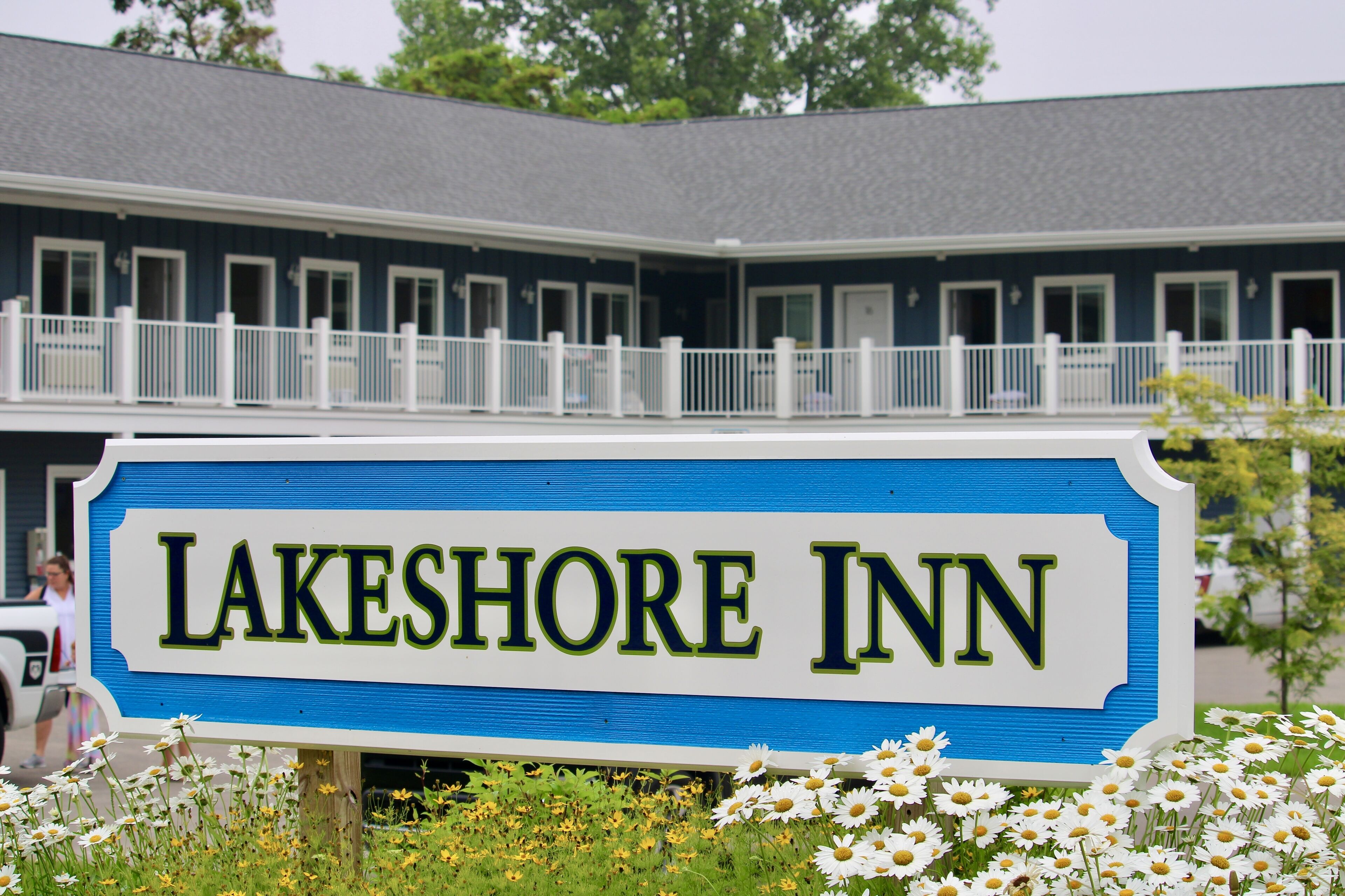 Letrero del Lakeshore Inn con un esquema de color azul y blanco, rodeado de flores blancas.