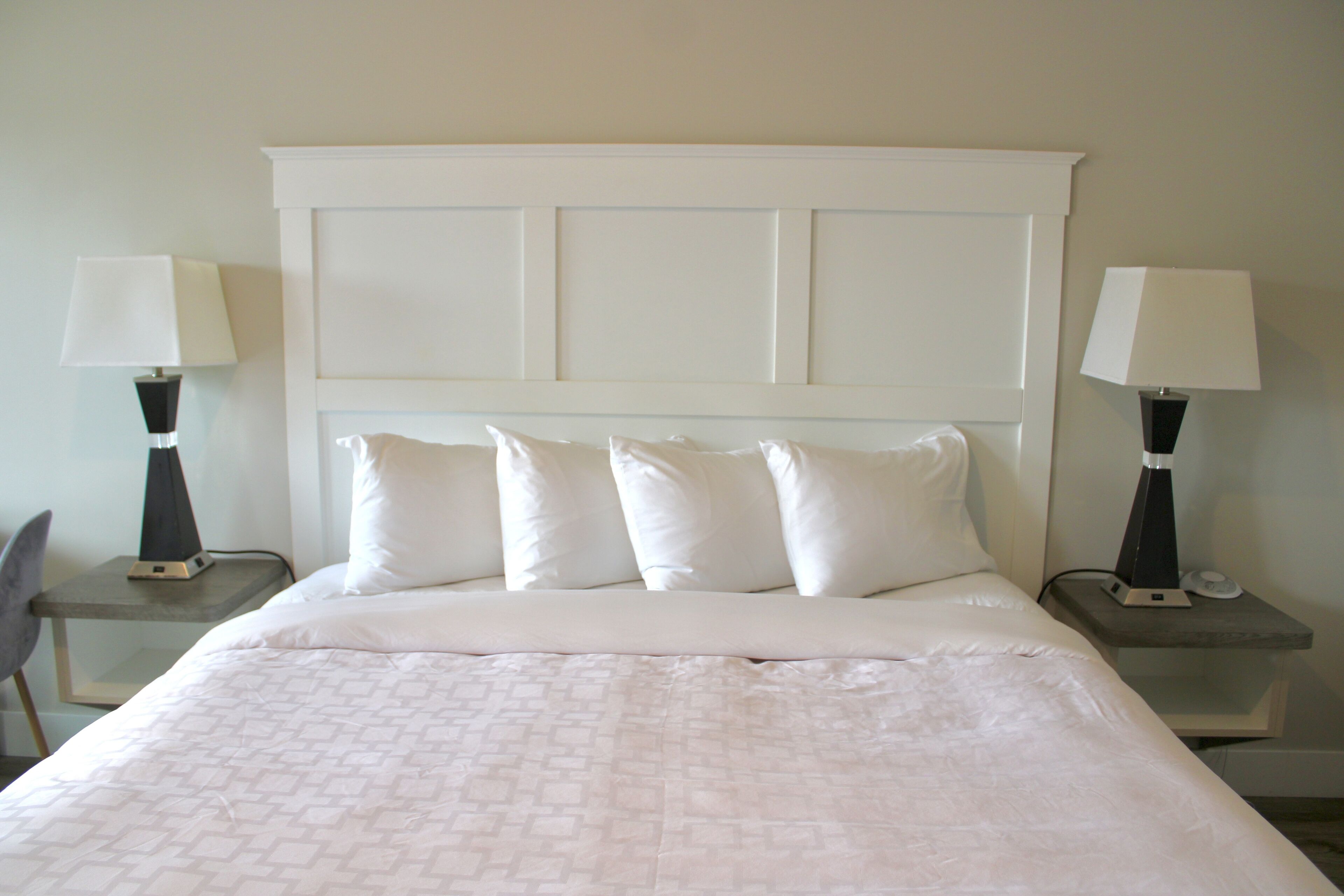A neatly made bed with a white headboard and four pillows, flanked by two bedside tables with lamps.