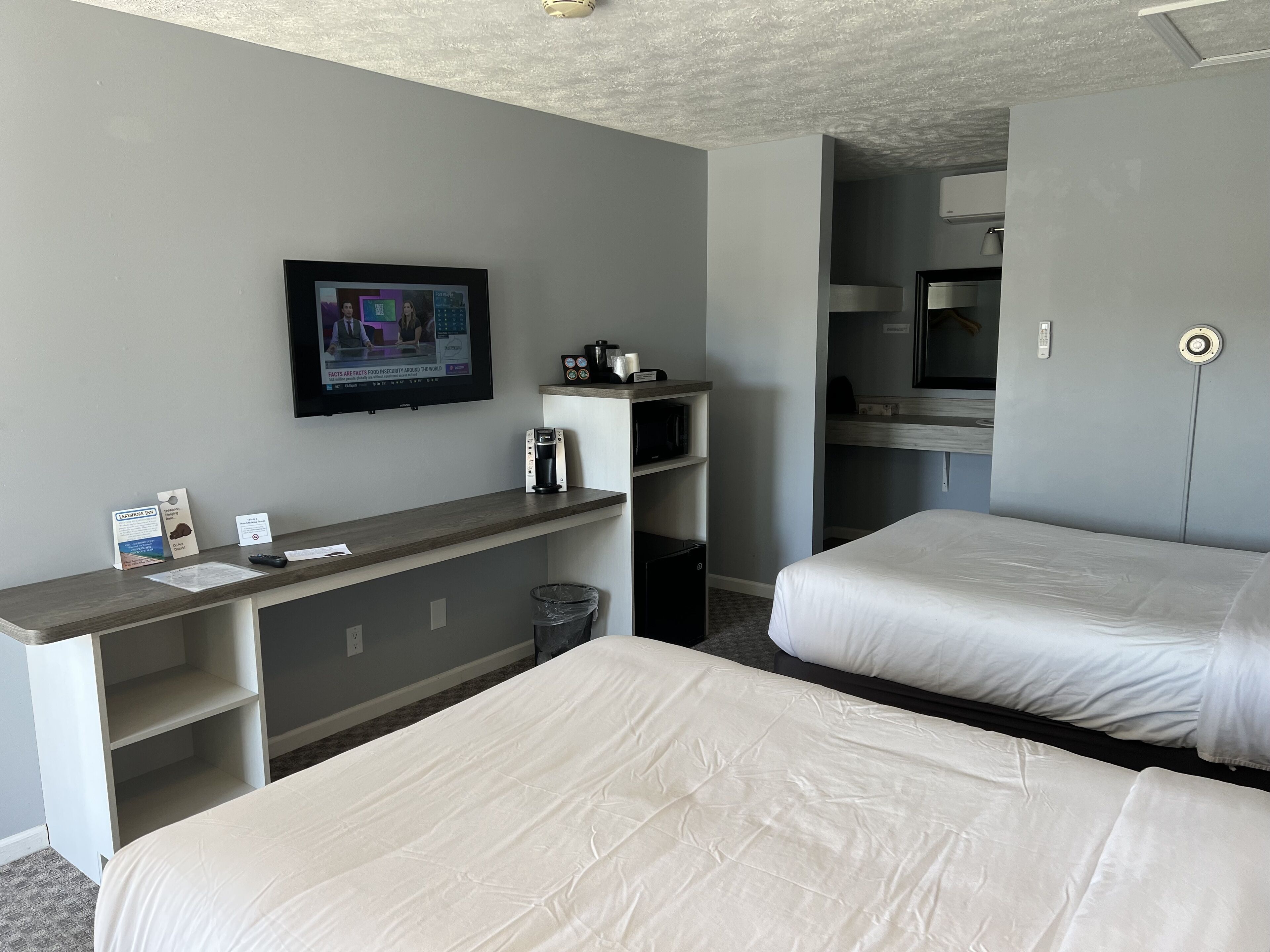 A hotel room with two beds, a TV mounted on the wall, a coffee machine, and a microwave.