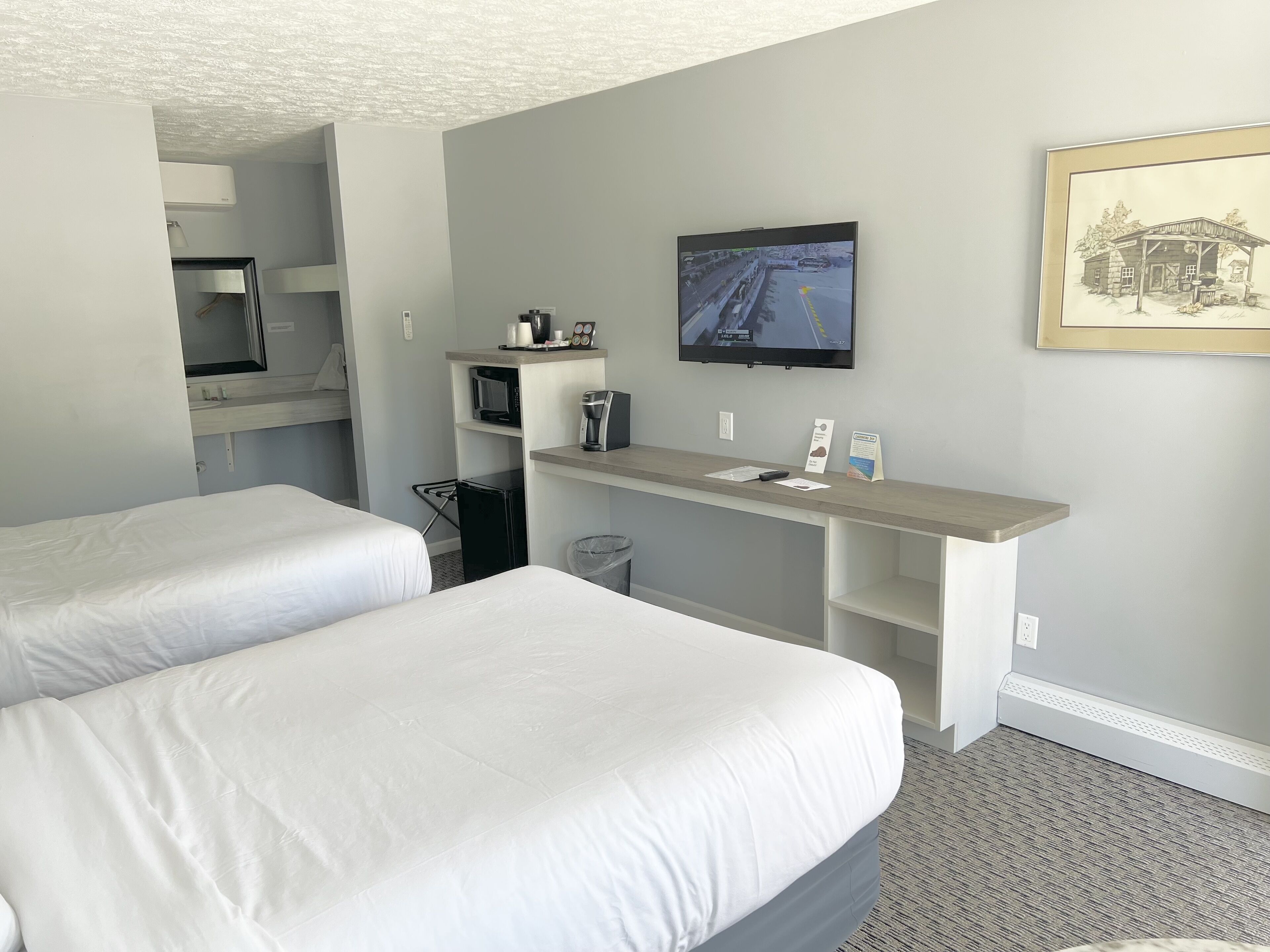 Une chambre d’hôtel avec deux lits, un bureau avec un ordinateur, une télévision et une petite kitchenette.