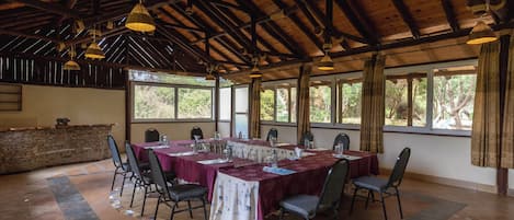 A large dining area with a long table set for a meal, surrounded by chairs, under a wooden ceiling with hanging lights.